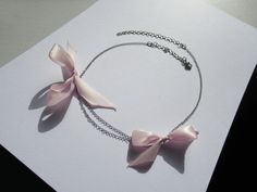 Rannka's dusty pink bow necklace with ribbons is a thoughtful romantic birthday gift and anniversary jewelry for a girlfriend. The silver jewelry piece is ideal for youth, and a charming summer elegant chain necklace.  𝐒𝐈𝐙𝐄: ➤ Adjustable Fits Circumference from 16″ - 20″ (40.6cm - 50.8cm)  𝐃𝐄𝐓𝐀𝐈𝐋𝐒: ➤ Materials: Stainless Steel, Ribbon ➤ Ready to Ship -The Rannka Bow Necklace features two dusty pink ribbon bows and a double stainless steel chain design. -Great for a fun summer day and night.  𝐒𝐔𝐆𝐆𝐄𝐒𝐓𝐄𝐃 𝐂𝐀𝐑𝐄: Use water and a drop of mild detergent. Rinse, then line dry. Always make sure to wipe off water and dry your jewelry completely after cleaning. Do not use any products containing alcohol. Be sure to take off your jewelry before swimming, showering, etc.  𝐂𝐎𝐎? Pink Ribbon Jewelry As Gift, Pink Ribbon Jewelry Gift, Pink Ribbon Jewelry For Gifts, Pink Ribbon Wedding Jewelry, Silver Ribbon Necklace For Gift, Pink Bow Jewelry Gift, Pink Bow Necklace For Party, Adjustable Necklace With Decorative Bow As Gift, Adjustable Necklace With Decorative Bow For Gifts