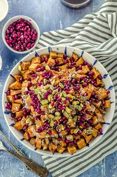 a bowl filled with sweet potatoes and pomegranates next to two bowls of nuts