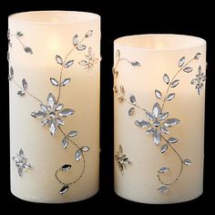 two white candles are decorated with silver leaves and flowers on them, one candle is lit