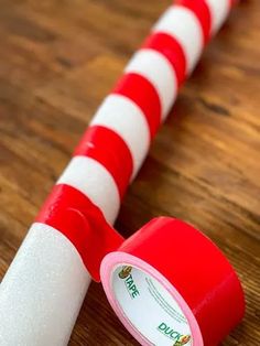 a red and white striped tape on top of a wooden table next to a roll of toilet paper