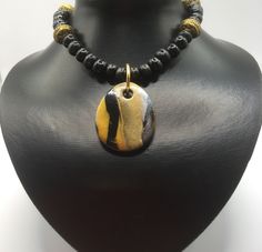 I've used the Japanese  technique mokume gane to create this polymer clay pendant. It comprises gold, white and black polymer clay. The pendant has been teamed with black wooden beads and golden spacer beads. The necklace is closed with a lobster claw lock and extends to 48cm if using the extender chain. The pendant measures 4.2 x 3.5cm. For more jewellery in similar colours, see the polymer clay section. Handmade Polymer Clay Pendant Necklace, Gold Carved Round Pendant Necklace, Handmade Gold Polymer Clay Jewelry, Unique Gold Polymer Clay Jewelry, Spiritual Polymer Clay Pendant Necklace, Gold Medallion Necklace With Carved Details, Unique Gold Polymer Clay Necklace, Handmade Polymer Clay Round Pendant Necklace, Handmade Round Polymer Clay Pendant Necklace