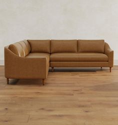 a brown leather couch sitting on top of a hard wood floor next to a white wall