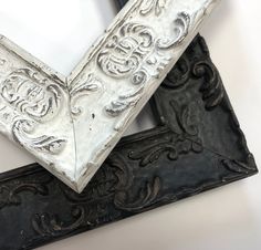 two ornate silver and black frames sitting on top of a white table next to each other