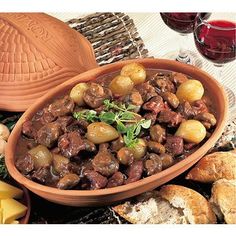 a bowl filled with meat and potatoes on top of a table next to some bread