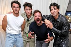 four men posing for the camera in front of a white curtain with their hands up