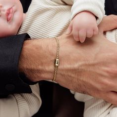 a man holding a baby in his arms with a gold bracelet on it's wrist