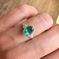 a woman's hand holding a ring with an emerald and three diamonds on it