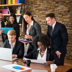 a group of people standing around a table with laptops and papers in front of them