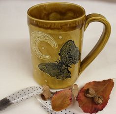 a coffee cup sitting on top of a table next to a knife and some leaves