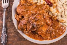 a white plate topped with meat covered in gravy next to a fork and knife