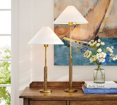 a lamp and some books on a wooden table in front of a painting with flowers