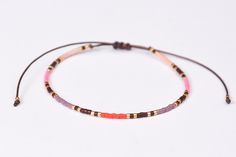 two bracelets with beads and cord on white background, one is pink and the other is brown