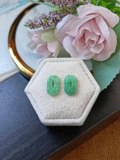 two green earrings sitting on top of a table next to a pink flower and vase