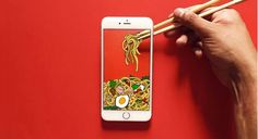 a person holding chopsticks next to an iphone with noodles and egg on it