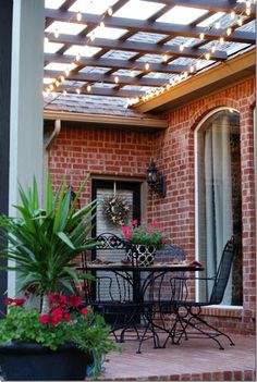 a patio covered in lights and potted plants next to a brick building with an awning