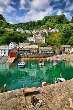 boats are docked in the water near houses on a hill side with green hills behind them