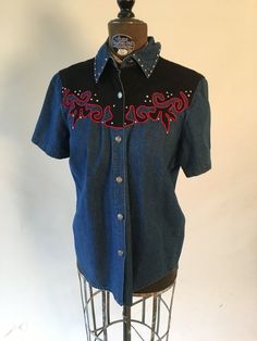 1990's Rhythm Blue short sleeve denim shirt with red and black western details and silver studsBust: 40"Waist: 39"Shoulder to hem: 27" Blue Vintage Western Style Tops, Denim Blue Button-up Top For Rodeo, Navy Blue Western Shirt, Red Velvet Shirt, Vintage Denim Blue Button-up Top, Denim Blue Western Button-up Tops, Short Sleeve Denim Shirt, Daphne Costume, Studded Shirt