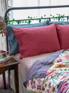 a bed with pink and blue pillows on top of it next to a small table