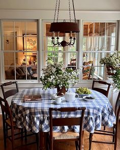 a dining room table with blue and white checkered cloth on it, surrounded by windows