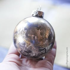 a hand holding a silver ornament in it's left hand, showing the top part