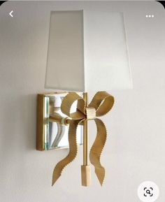 a white lamp with a gold bow on the wall next to a light fixture that is attached to a wall