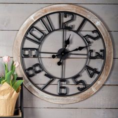 a large metal clock sitting on top of a wooden wall next to a vase with flowers