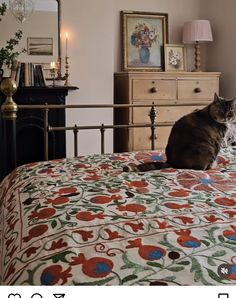 a cat sitting on top of a bed next to a dresser and lamp in a bedroom