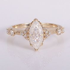 a white diamond ring with gold band and diamonds on the sides, sitting on a white surface