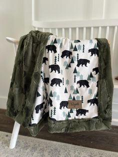 a green and white blanket with black bears on it, sitting next to a chair