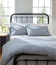 a bed with blue and white checkered sheets in front of two windows, next to a night stand