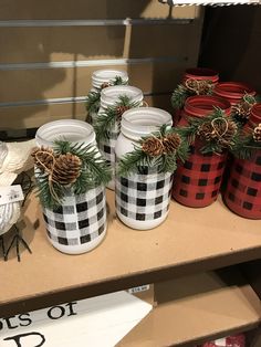 several jars with pine cones and evergreen branches in them sitting on a shelf next to other christmas decorations