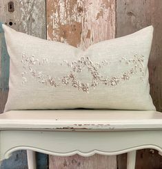 a white bench with a pillow on top of it and a wooden wall behind it