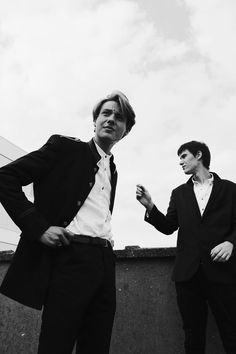 two men in suits standing next to each other on a roof with one holding his hand out