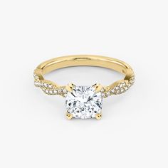 a yellow gold engagement ring with a cushion cut diamond and pave set diamonds around the band