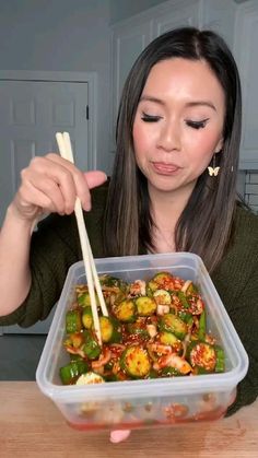 a woman holding chopsticks over a container of food with broccoli and peppers