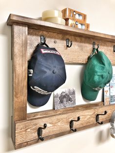 two hats are mounted to a wooden shelf with hooks on the bottom and one hat is hanging from it's side