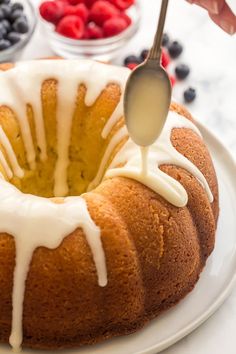 a bundt cake with white icing and berries on the side, being drizzled with cream cheese