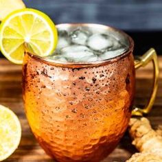 a copper mug filled with ice and lemons on top of a wooden table next to sliced ginger