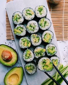 sushi rolls with avocado and chopsticks on a white tray next to bamboo mat