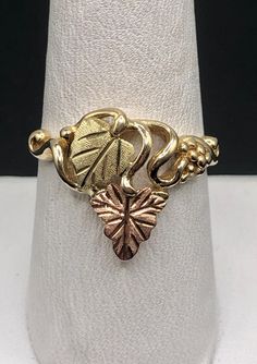 This is a lovely 10K Black Hills Gold ring with ubiquitous grape and leaf design. Ring features yellow gold grape clusters and leaves of pink and green gold. Head of ring measures 16.4mm (5/8"), band measures approximately 2.1mm at its narrowest. Stamped 10K with an indeterminate hallmark. SIZE 9 WEIGHT 4.0 grams FREE SHIPPING! Rose's Collectibles is a family-owned business with locations in Stillwater, MN and Lindstrom, MN. Visit us at rosescollectibles.com Black Hills Gold Rings, Black Hills Gold Jewelry, Black Hills Gold, Leaf Motif, Jewelry Lookbook, Disney Jewelry, Black Hills, Still Water, Green Gold