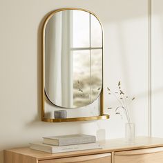 a mirror sitting on top of a wooden dresser next to a vase filled with flowers