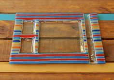 a wooden table topped with a colorful striped tray and two small pieces of glass on top of it