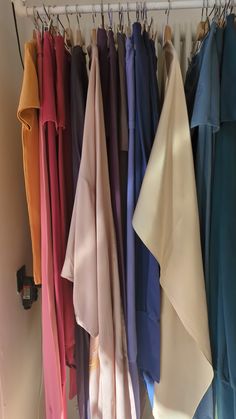 there are many different colors of cloths hanging on the clothes rack in this closet