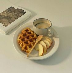 a white plate topped with waffles and apples next to a cup of coffee