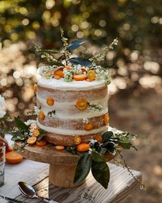 a wedding cake with oranges and greenery sits on a wooden table in the woods