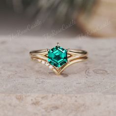 an emerald colored ring with diamond accents on it's sides, sitting on a stone surface