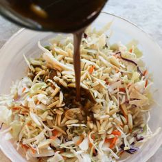 someone pours dressing into a bowl filled with coleslaw and shredded carrots