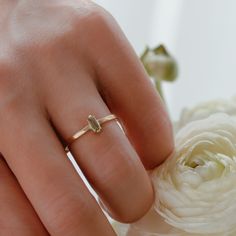 a woman's hand with a gold ring on her finger next to a white flower