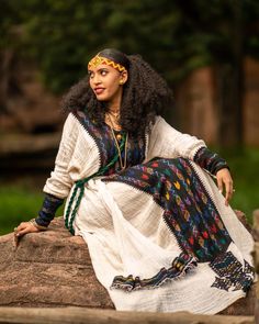 a woman sitting on top of a rock wearing a white dress and colorful head piece