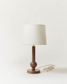 a wooden table lamp with a white shade on the base and a cord plugged into it